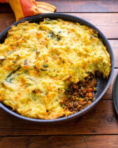 picture showing a skillet with mashed potatoes on top with a scoop out showing ground meat and carrots and peas